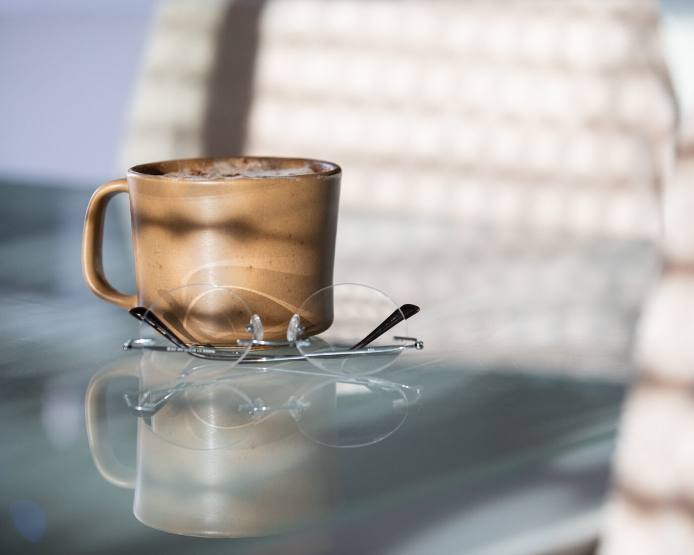 Ceramic mug and folded reading glasses on a reflective glass table
