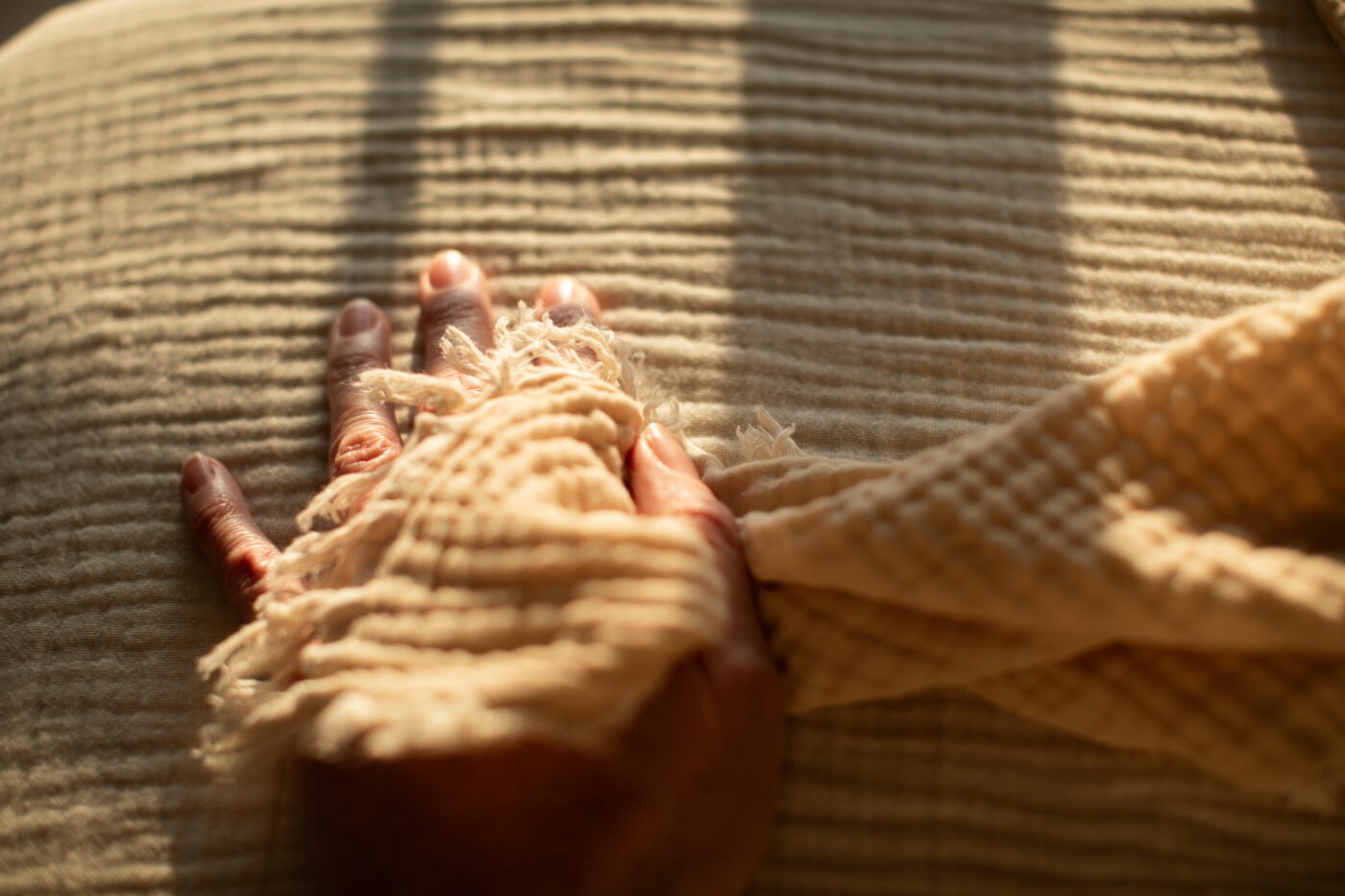 Hand touching the fringed edge of a woven blanket in sunlight
