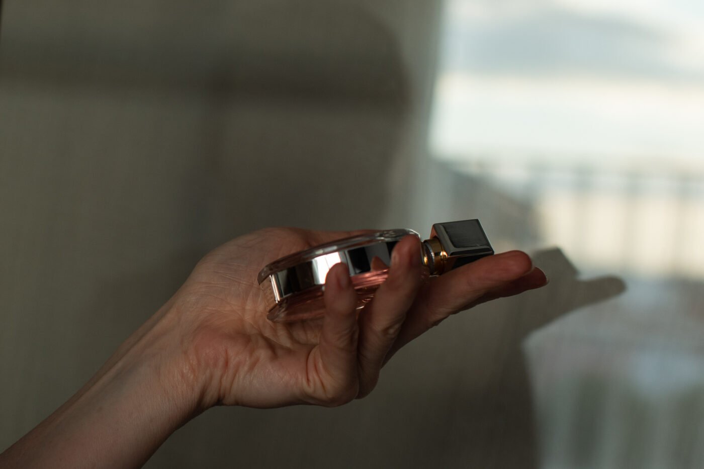 Hand holding a glass perfume bottle by a sunlit window