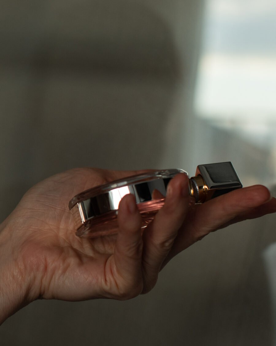 Hand holding a glass perfume bottle by a sunlit window