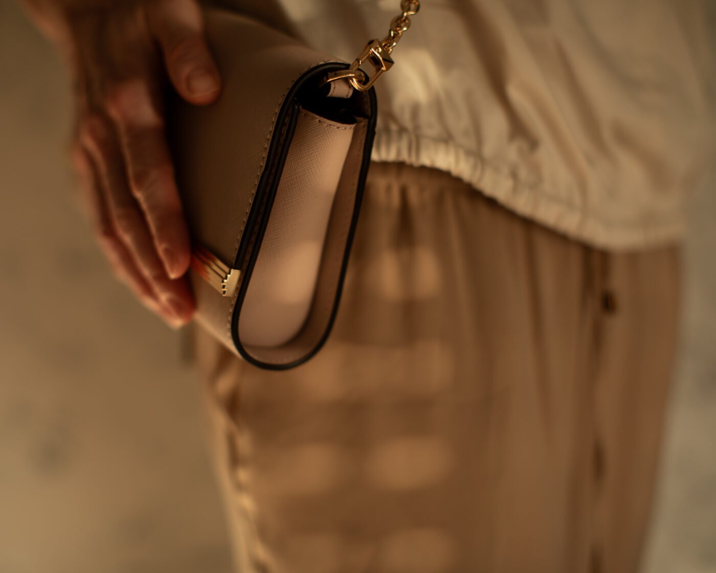 Hand holding a small clutch bag with gold chain hardware
