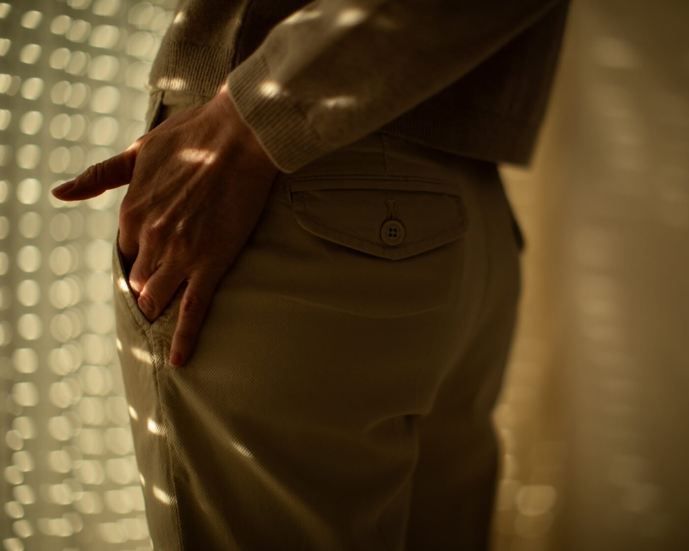 Hand tucked in a trouser back pocket in dappled light