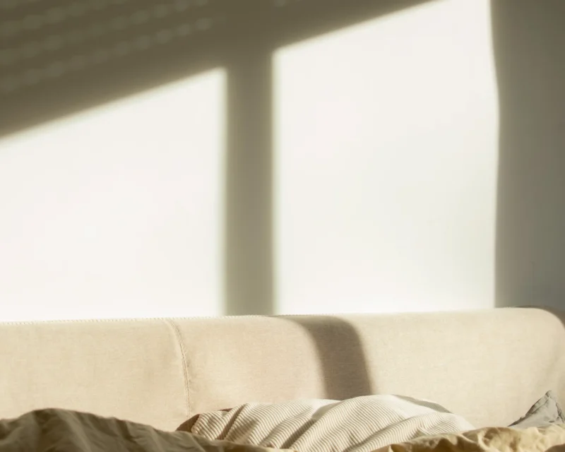 Afternoon window-light shadow falling across a bed and headboard