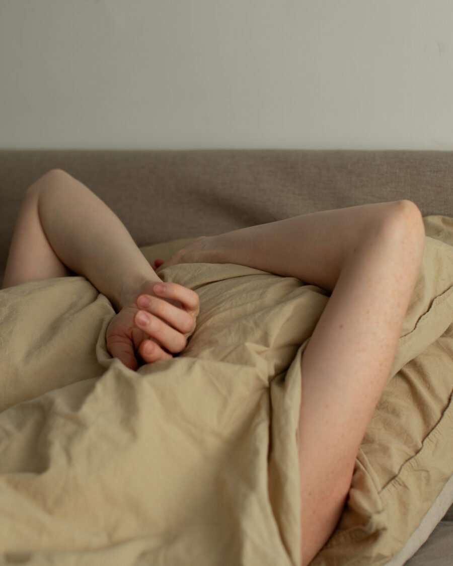 Close-up of tangled legs and a hand in rumpled bedsheets, soft morning light
