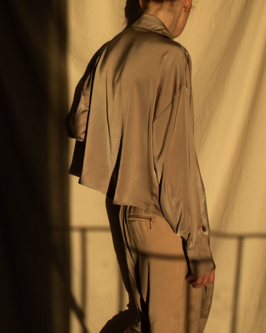 Woman seen from behind in a silky taupe blouse, golden late-afternoon light and railing shadow