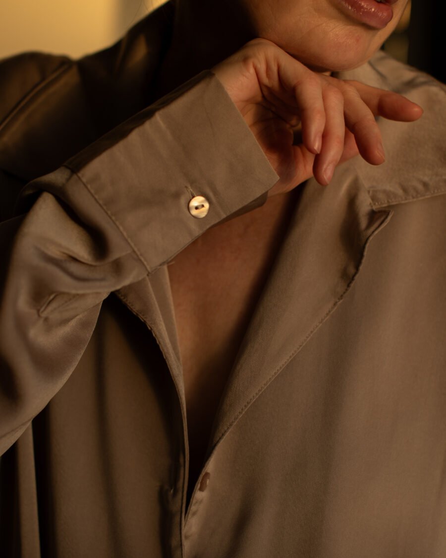 Close-up of a hand at the collar of a silky taupe blouse, warm light