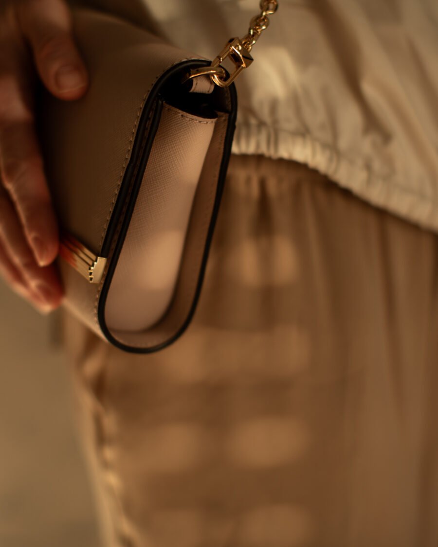 Close-up of a hand holding a taupe leather clutch with gold chain hardware